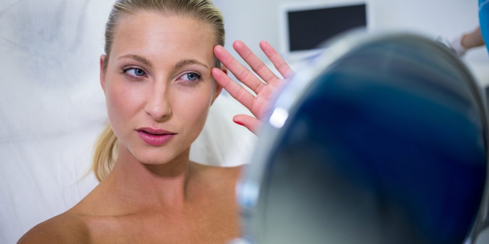 Happy woman checking her skin in the mirror after receiving cosmetic treatment